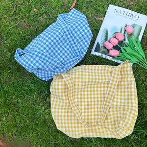 Blue and yellow plaid canvas tote bags displayed on green grass with tulips