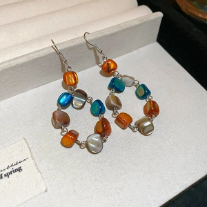 Détail de boucles d'oreilles pendantes colorées avec perles ambrées et blanches nacrées