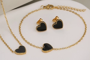 Detail view of gold stainless steel necklace bracelet and earrings with black heart enamel