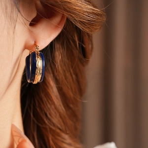 Primo piano di orecchini vintage a cerchio in smalto blu e oro indossati da una modella