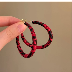 Détail de créoles géométriques faites à la main avec un enroulement de fibres rouge et noir