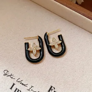Macro shot of U-shaped black enamel earrings featuring a gold flower motif with crystals