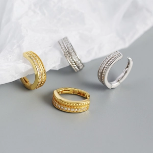 Close-up of gold and silver huggie earrings with layered crystal pavé and twisted textures
