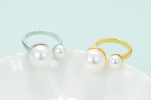 Elegant gold and silver open rings with two white pearls on a ceramic dish background