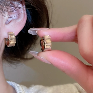 Detailed view of gold earrings with three step-cut clear zircons on a model's ear