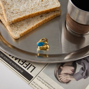 Detail of a gold stainless steel ring with turquoise stone on a rustic metal tray