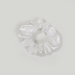 Minimalist white satin scrunchie with glossy pleated texture on light background