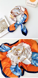 Detail of silk square scarf featuring a white floral pattern on a bright orange background