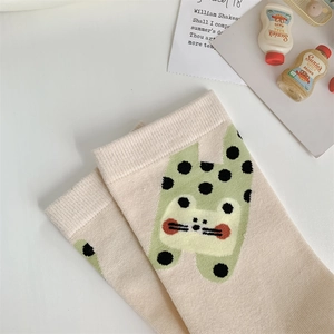 Close-up of beige knitted socks with cute green cartoon cat pattern on a white desk
