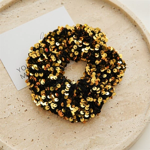 Close-up of black elastic scrunchie with shiny gold sequins on a beige ceramic plate