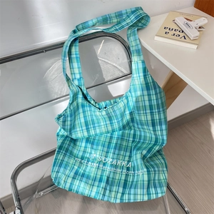 Detail of teal and blue checkered canvas tote bag with wide strap on acrylic chair