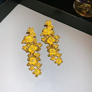 Gros plan de boucles d'oreilles dorées avec motif floral multicouche sur un plateau gris