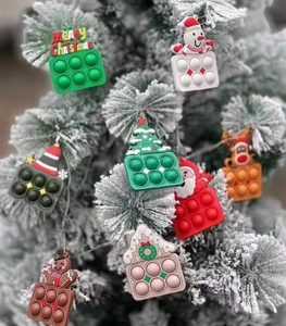 Dettaglio di giocattoli pop-it natalizi in silicone appesi a un ramo d'albero innevato