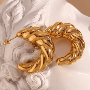 Macro shot of gold-plated croissant hoop earrings on a white artistic plaster background