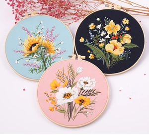 Three floral DIY embroidery kits in blue, black and pink displayed with wooden hoops