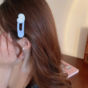 Détail d'une pince à cheveux bleu clair et d'une boucle d'oreille perle assortie portée