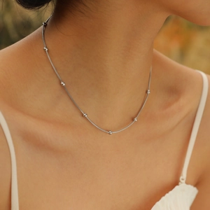 Close-up of minimalist stainless steel bead necklace worn by a model in warm light