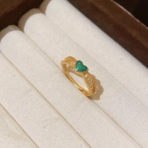 Macro detail of 24k gold plated ring with green heart element in a velvet jewelry box