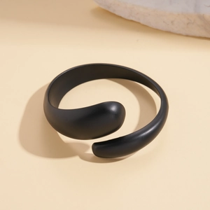 Detail view of a matte black irregular geometric open bangle on a beige stone display