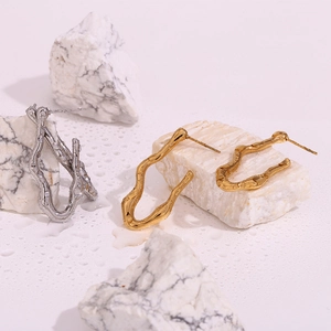 Detailed view of wavy V-shaped stainless steel earrings in gold and silver on white marble