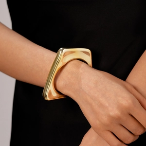 Close-up of a wide polished gold irregular geometric cuff bracelet on a model's wrist