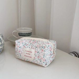 Quilted floral makeup bag with pink flower patterns and zipper closure on a white desk