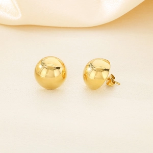 Macro shot of minimalist gold spherical stud earrings on soft beige silk background