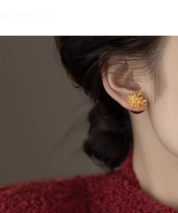 Macro detail of golden flower stud earrings with sparkling diamonds on female model