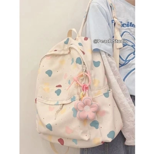 Detail view of cream canvas backpack with colorful abstract prints and pink plush flower charm