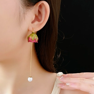 Détail de boucles d'oreilles rose séchée avec chaîne dorée et perle sur un mannequin