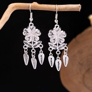 Macro detail of vintage silver flower earrings with hollow petals and leaf tassels on wood