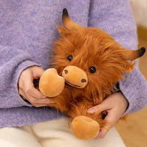 Cute highland cow plush toy with fluffy brown fur and horns held by a model