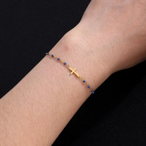 Cross pendant bracelet with gold chain and dark blue beads worn on a female wrist