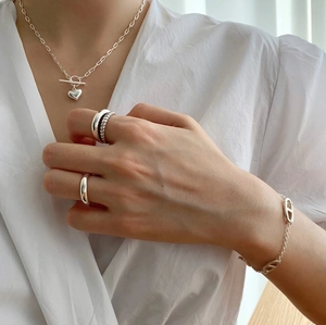 Detail of 925 sterling silver heart pendant necklace and layered twisted rings on model