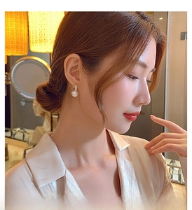 Close-up of elegant gold pearl drop earrings worn by a model in a warm setting