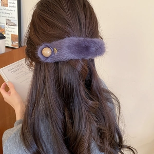 Detail view of purple plush faux fur hair clip with beige pearl accent on wavy hair