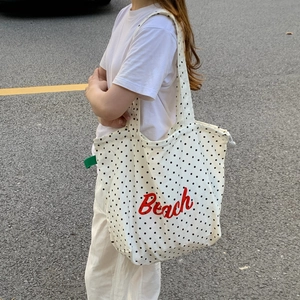 Detail einer weißen Polka-Dot-Stofftasche mit rotem Beach-Schriftzug und Schultergurt