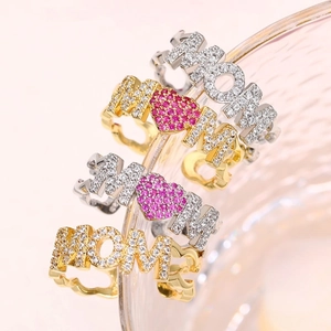 Close-up of MOM letter rings with micro-set zircons and pink heart on wavy metal bands