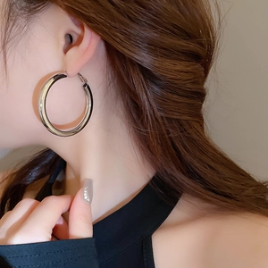 Detail view of large polished silver hoop earrings worn by a model on a neutral background