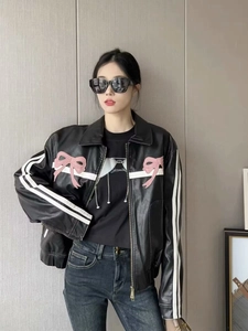 Détail d'une veste en cuir noir avec un nœud rose et des rayures blanches sur les manches
