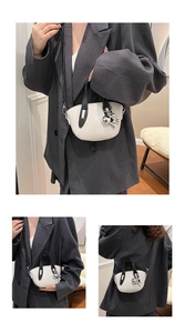 Détail d'un sac à main blanc avec poignées noires et pendentif ours en métal argenté