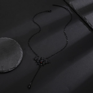Gothic black bat necklace with red gemstone and teardrop pendant on stone surface