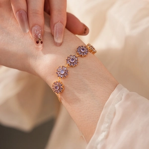 Macro detail of a gold-plated bracelet featuring five purple zircon floral pendants