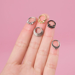 Detail view of steel bat and layered hoop nose rings held against pink backdrop