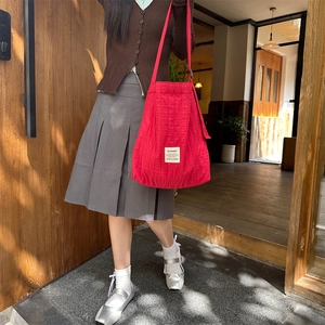 Detail of red quilted canvas shoulder bag featuring a white brand label and soft texture