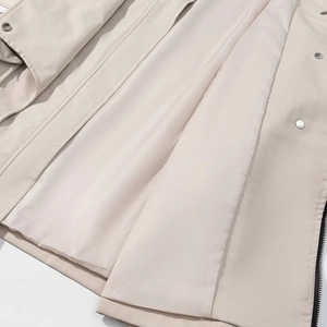 Detail view of cream trench coat lining with metal snaps and black zipper edge