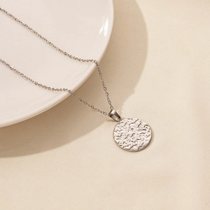 Detail of silver round pendant with hammered lava texture on a minimalist chain