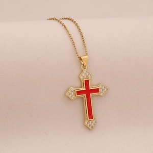 Détail macro d'un collier croix doré avec centre rouge et petits diamants étincelants
