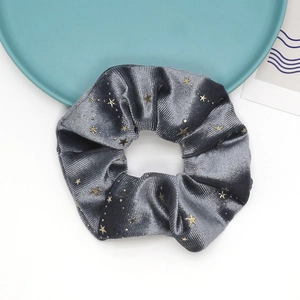 Detail of dark grey velvet scrunchie featuring golden star patterns on white background