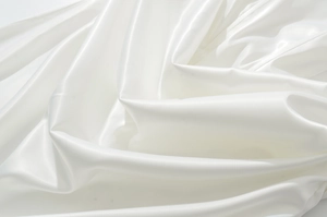 Gros plan du tissu en satin blanc montrant une texture brillante et un drapé plissé